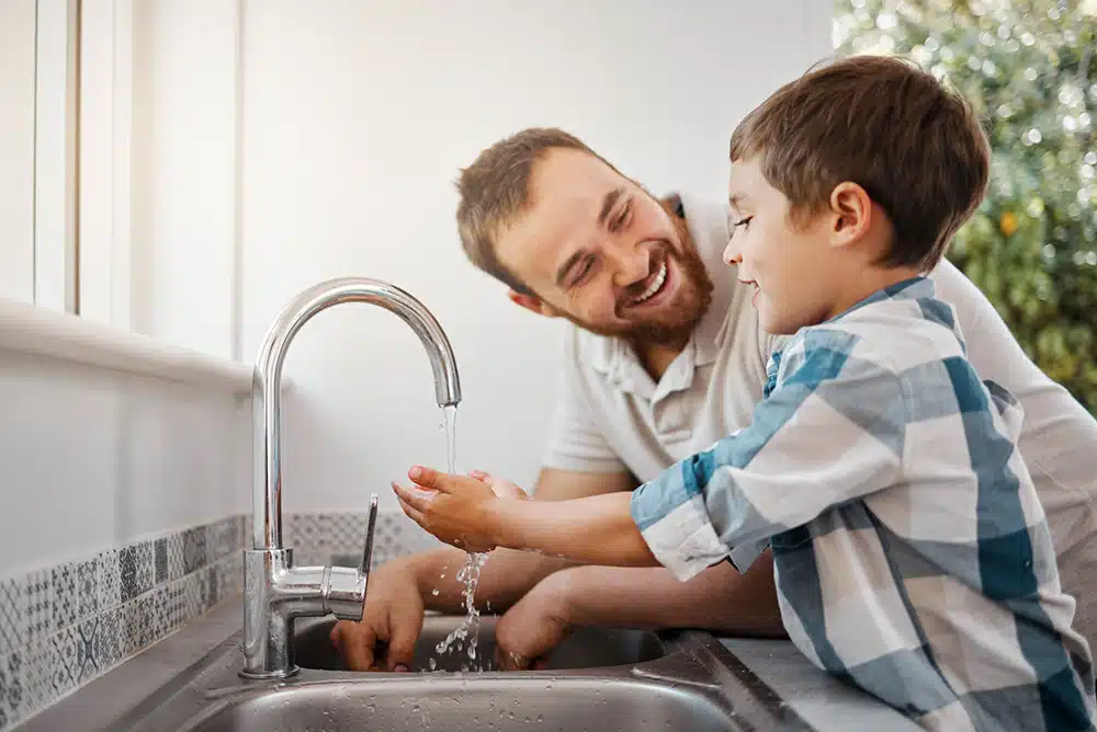 Father helping son wash hands in residential kitchen sink.